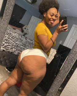 Curvy woman in yellow top and white thong takes mirror selfie, showing backside in bedroom setting.