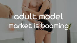 A woman in black lingerie is embracing a shirtless man in white pants in a modern bathroom setting.