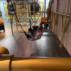 An empty leather swing suspended by chains in a room with golden metal framing and wooden flooring.