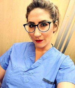 Woman in blue scrubs and glasses with red lipstick.