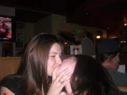 Two women in a dimly lit bar, one kissing the other's neck.
