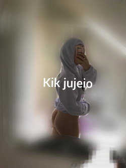 Person in a gray hoodie taking a mirror selfie, showing bare midriff and lower back, standing in a softly lit room.