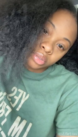 A Black woman with curly hair wearing a green sweatshirt lies down, looking at the camera in a casual indoor setting.