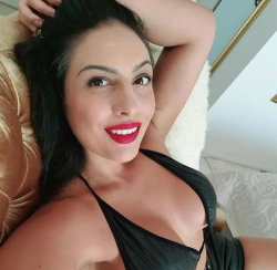 Brunette woman with red lipstick smiles at the camera, lying on a plush surface in a black halter top.