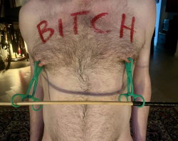 A shirtless man with chest hair has the word 'BITCH' written in red on his chest.