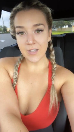 Blonde woman with braided hair in a red top, sitting in a car, taking a selfie.