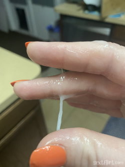 Close-up of a hand with orange nail polish, showing a white viscous substance dripping between fingers in an indoor