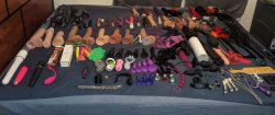 Various adult toys and accessories laid out on a blue tablecloth, including vibrators, dildos, restraints, and other