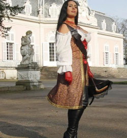 Brunette woman in a steampunk-inspired outfit with off-shoulder blouse, patterned vest, red gloves, and thigh-high