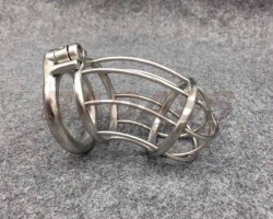 A metallic cage-style chastity device with a ring and locking mechanism, resting on a gray textured surface.