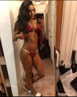 Curvy woman with long dark hair in a sparkly red bikini takes a mirror selfie in a narrow hallway, wearing white heels.
