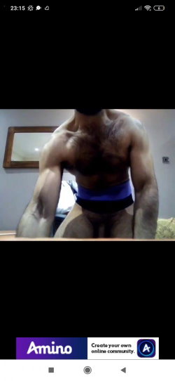 Muscular man with hairy chest and arms, wearing blue underwear, posing in front of a mirror in a room.