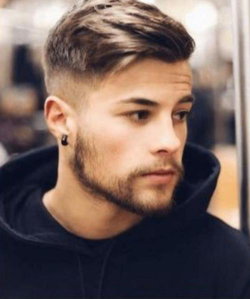 Man with short styled hair and beard wearing a black hoodie, looking off to the side in an indoor setting.
