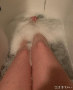 Close-up selfie of legs and feet in a bubble bath, with hands visible in soapy water.
