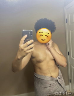 Shirtless person with curly hair taking a mirror selfie, wrapped in a towel, in a bathroom setting.