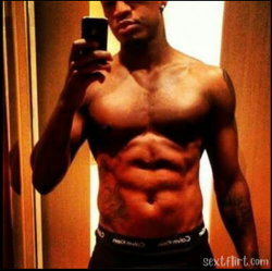 Shirtless muscular man with defined abs and tattoos takes mirror selfie in dimly lit room wearing black Calvin Klein