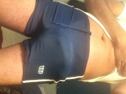 Person wearing navy blue athletic shorts and a white top, lying on their side with arm visible, in a casual indoor
