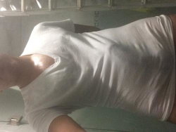 Person in a white t-shirt, lying on their side with arm visible, in a dimly lit indoor setting.