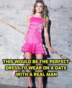 A young woman with long blonde hair wears a bright pink velvet mini dress with ruffles, standing against a weathered