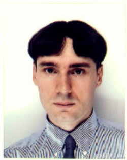 Man with dark hair and a striped shirt, wearing a tie, facing forward against a plain background.