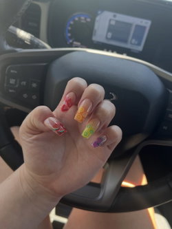 Close-up of a hand with colorful fruit-themed nail art, resting near a car steering wheel.