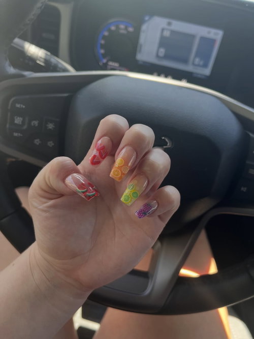 Close-up of a hand with colorful fruit-themed nail art, resting near a car steering wheel.