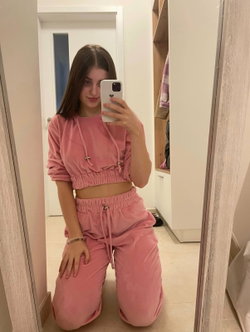 A brunette woman in a pink matching crop top and pants set poses in a mirror selfie.