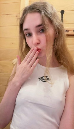 Blonde woman in a white top poses with hand near mouth.