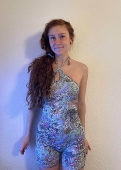 Redheaded woman with curly hair in a colorful patterned one-piece swimsuit, standing against a plain wall.