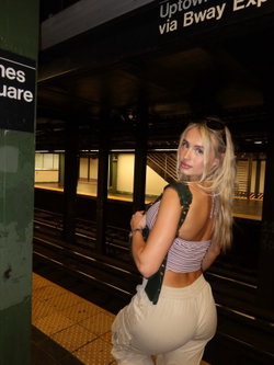 Blonde woman in a striped crop top and white pants poses in a subway station.