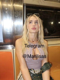 Blonde woman in striped top and green jacket sitting on a train.