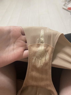 Close-up of a hand holding beige lingerie with visible wear and residue, showing skin and fabric texture.
