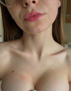 Close-up of a woman with brown hair, glasses, and nose ring, bare chest visible, indoors.