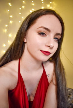 A woman with long brown hair and red lipstick wears a red top in a festive setting.
