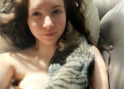 Woman with brunette hair cuddles a cat on a couch.