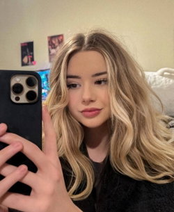 Blonde woman with wavy hair taking a selfie in a bedroom.