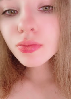 Close-up of a blonde woman with soft makeup, glossy lips, and visible shoulders, likely taken in a selfie style.