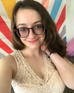 A woman with brown hair and glasses smiles in a lace top, posing in front of a colorful striped backdrop.