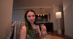 A person with green hair sits on a couch holding a clear object.