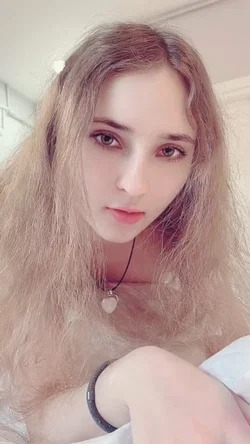 A person with long, wavy hair and a necklace poses in a selfie.