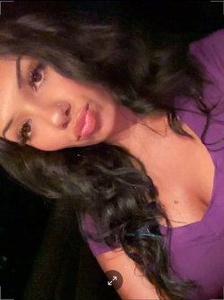 Woman with long dark curly hair wearing a purple top, lying down in a dimly lit setting.