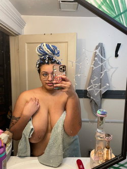 Curvy woman with braided updo holds a towel while taking a bathroom mirror selfie.
