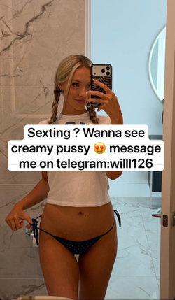 Blonde woman in white crop top and black thong takes mirror selfie in marble bathroom, holding phone with zebra case.