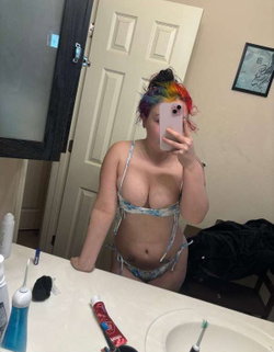 Person with rainbow hair in a blue bikini taking a selfie in a bathroom.