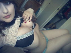 Brunette woman in black lace bra and light blue underwear, lying down with hand on chest, taking a close-up selfie