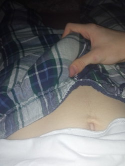 Close-up of a person's midsection with plaid pajama pants being pulled down, revealing part of the stomach and waist