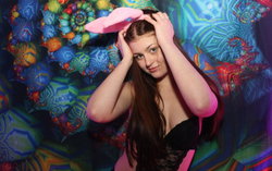A woman with long brown hair and a black top poses playfully with a pink bunny mask.