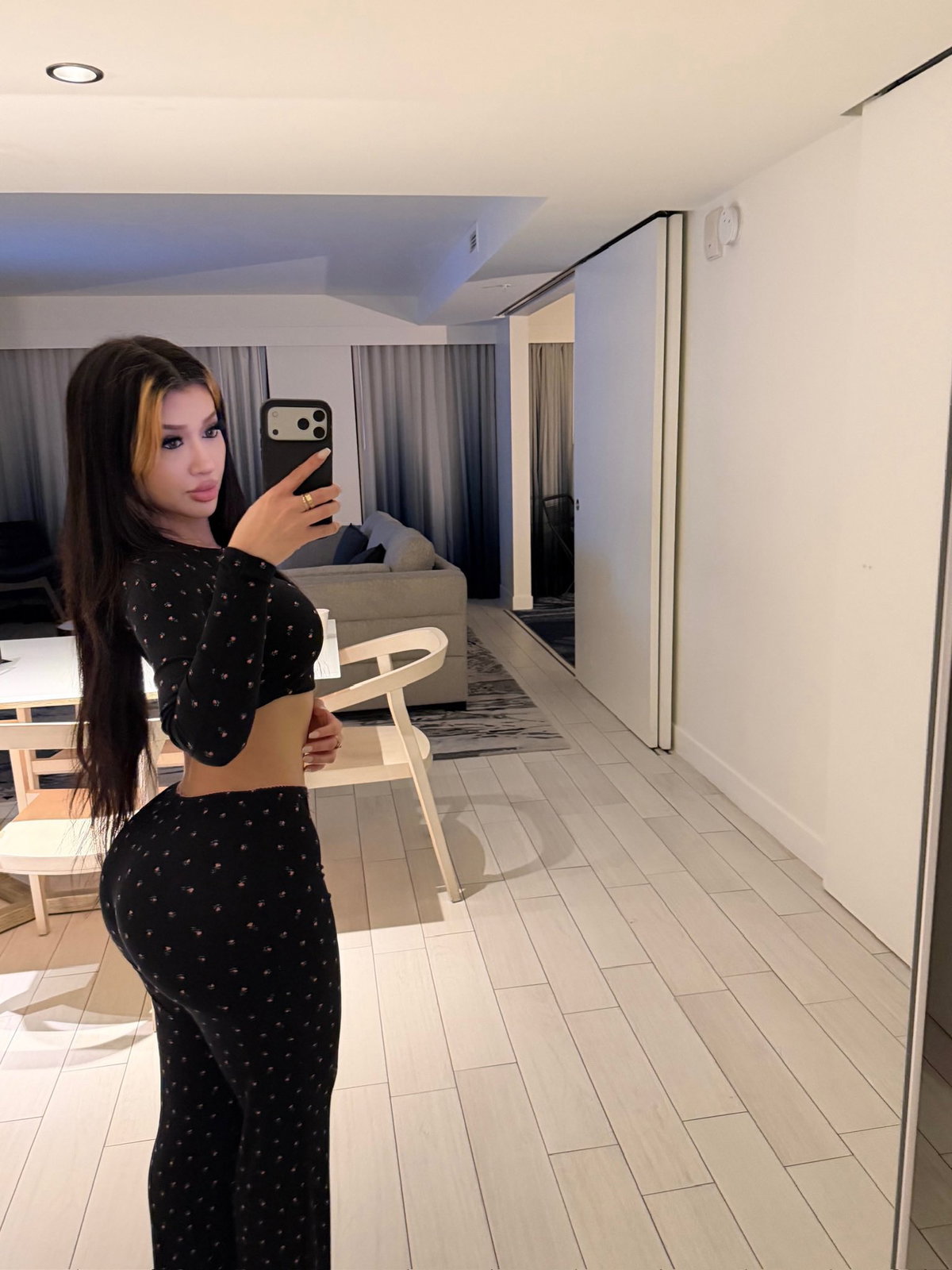 Curvy woman with long dark hair and blonde highlights takes a mirror selfie in a black patterned crop top and matching