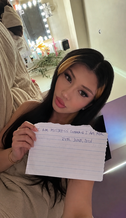 Woman with long dark hair and bangs holds a notepad in a well-lit room.