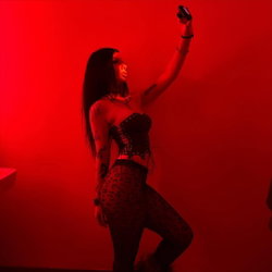 Brunette woman with tattoos in a corset and patterned leggings takes a selfie under red lighting.